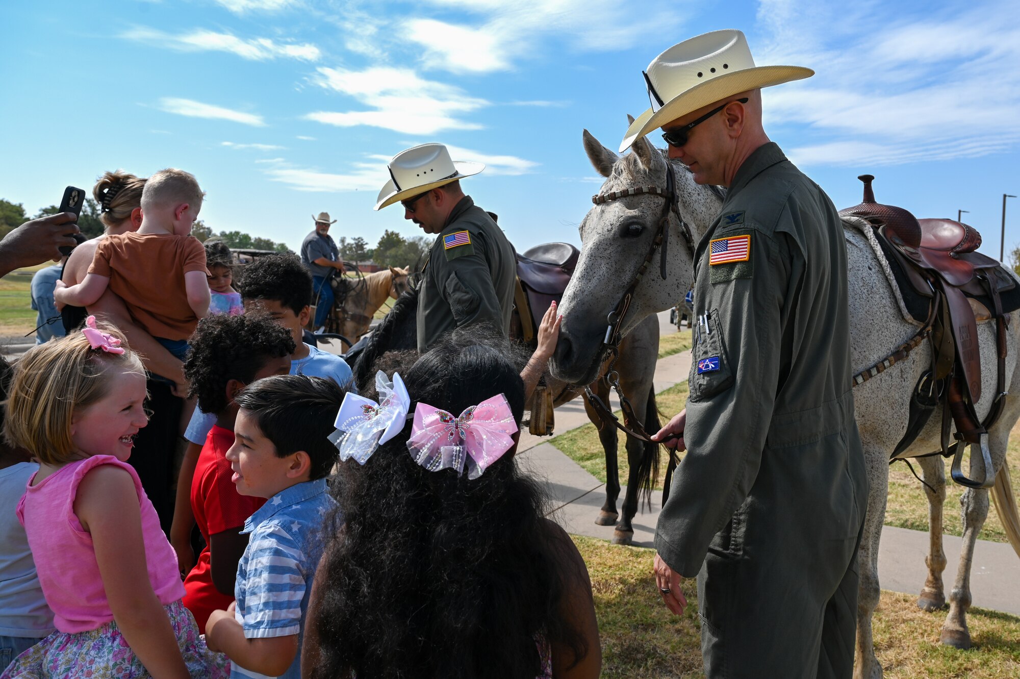 U.S. Air Force Col. Jeff Marshall, 97th Air Mobility Wing commander, and Chief Master Sgt. Justin Brundage, 97th Air Mobility Wing command chief, invite children from L. Mendel Rivers Elementary School to pet the horses at Altus Air Force Base, Oklahoma, during the 26th Annual Cattle Drive, Aug. 22, 2024. Children on base are able to pet horses, meet with community members and Airmen running the cattle drive. (U.S. Air Force photo by Senior Airman Kari Degraffenreed)