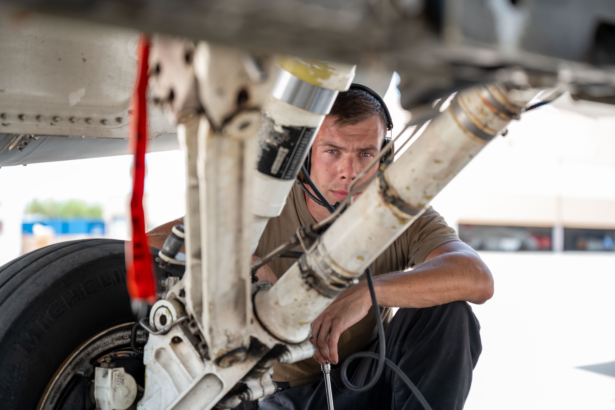 A man looks at the camera kneeling down by a landing gear.