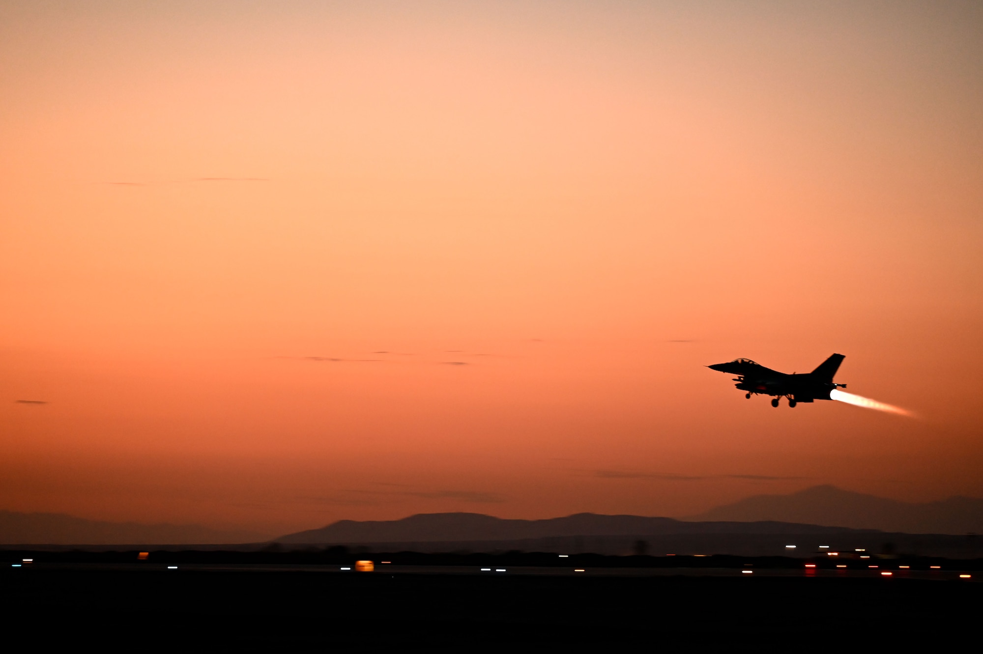 A plane takes off in front of an orange sky.