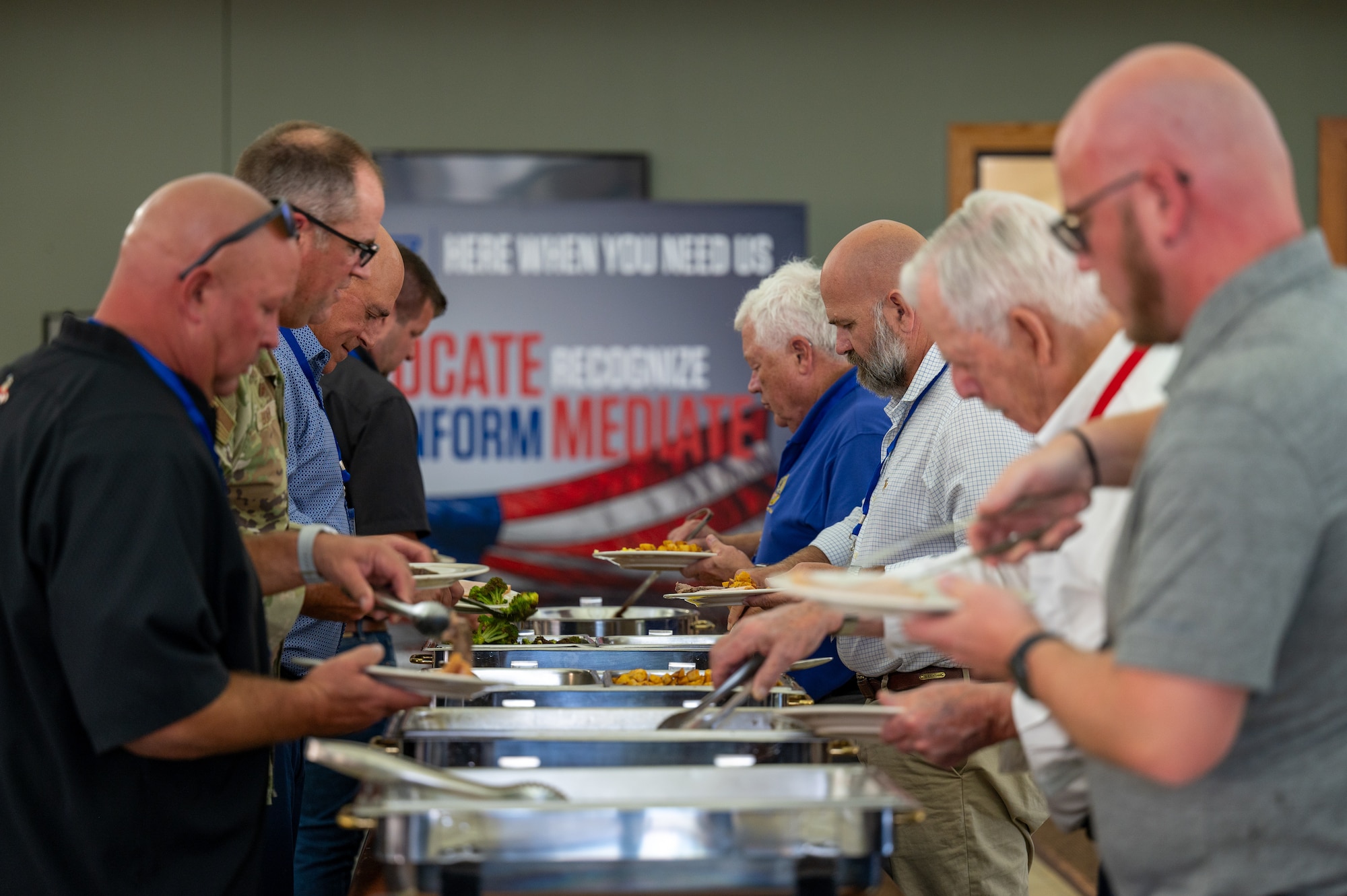 Men and women fill their plates with food. In the background, a banner for the Employer Support of the Guard and Reserve.