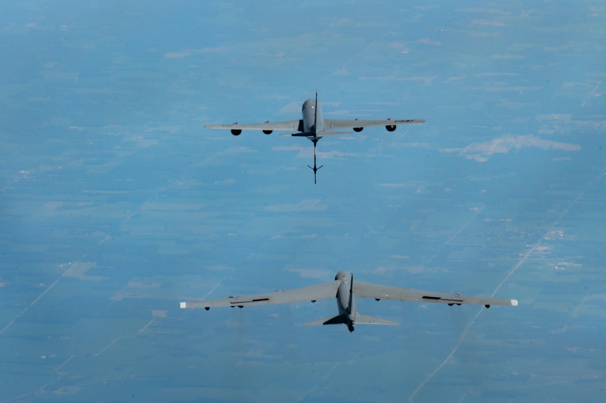 Two military aircraft fly near one another. The top is a KC-135 Stratotanker and the other is a B-52 Stratofortress.