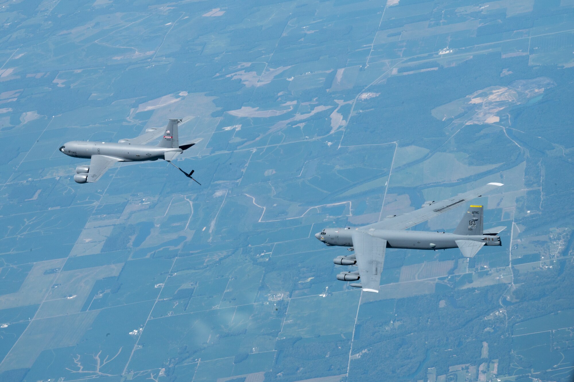 Two military aircraft fly near each other. The back one is a B-52 and the front on is a KC-135.