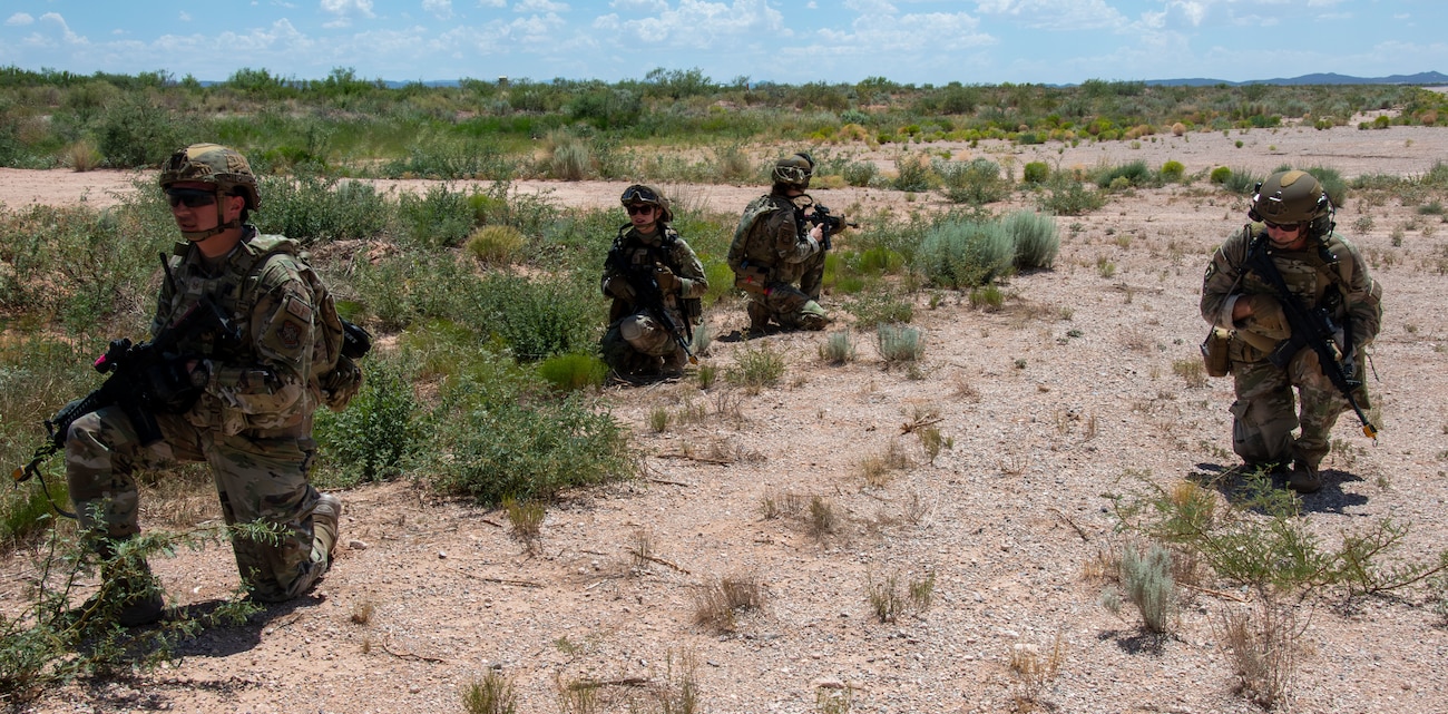 Four Airmen kneeling down in the desert during a training exercise