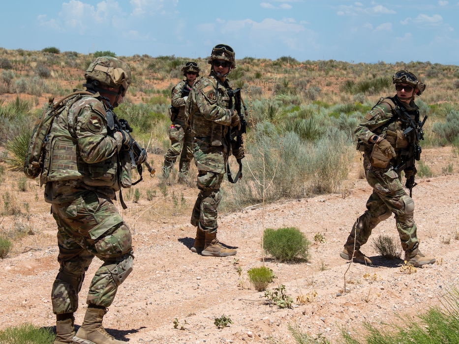 Three Airmen walk across a clearing in the desert during a training exercise