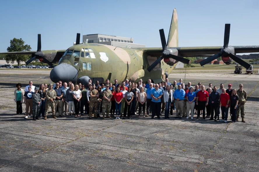 People standing in front of C-130 plane at Air Force base.