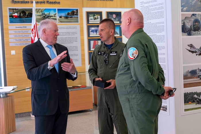 A man in a suit talks with two Polish Air Force pilots in a room filled with historical and informational displays