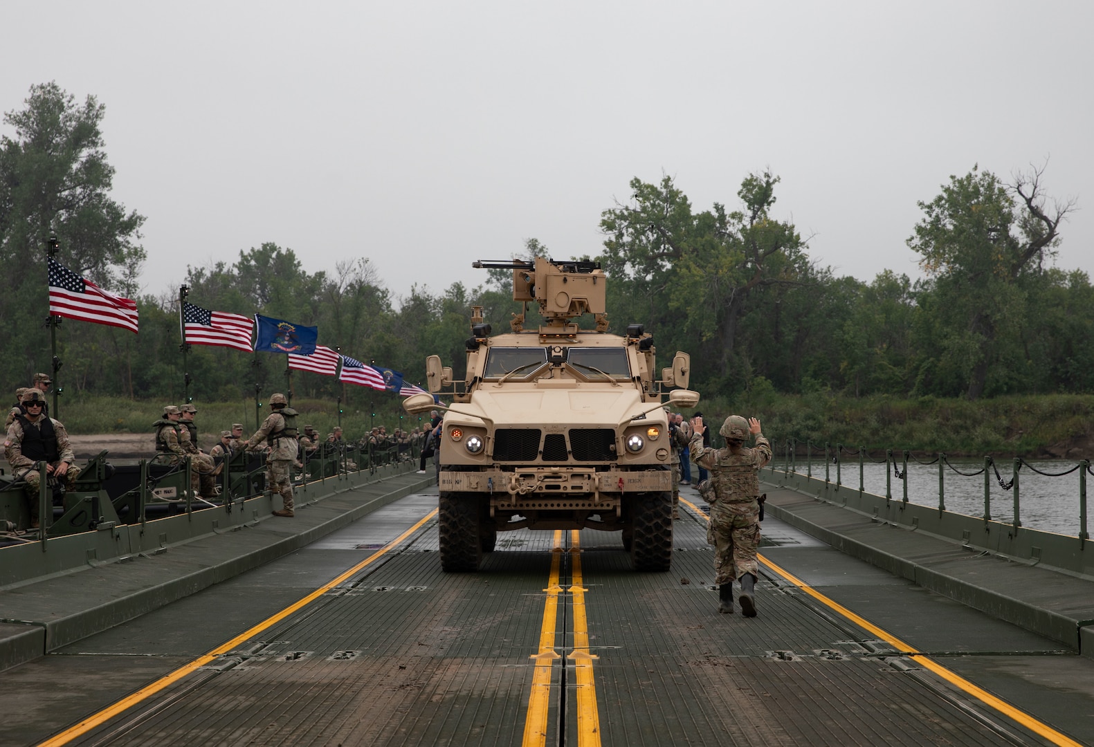 A Soldier with the 131st Military Police Battalion, North Dakota Army National Guard, guides the driver of a Mine-Resistant Ambush Protected All-Terrain Vehicle across a floating bridge during a wet gap crossing training exercise on the Missouri River near Kimball Bottoms, North Dakota, Aug. 17, 2024. The bridge was constructed by the 957th Multi-role Bridge Company.