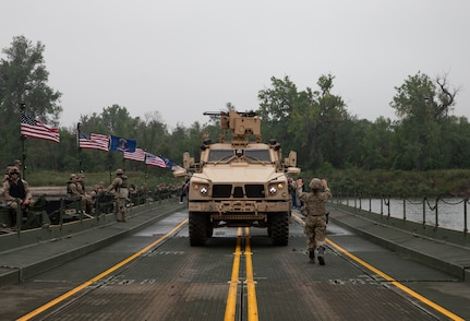 A Soldier with the 131st Military Police Battalion, North Dakota Army National Guard, guides the driver of a Mine-Resistant Ambush Protected All-Terrain Vehicle across a floating bridge during a wet gap crossing training exercise on the Missouri River near Kimball Bottoms, North Dakota, Aug. 17, 2024. The bridge was constructed by the 957th Multi-role Bridge Company.