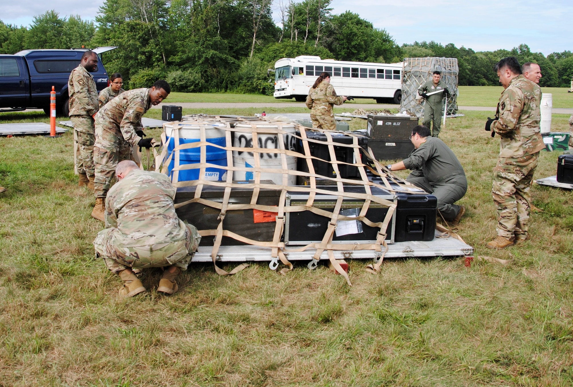 Citizen Airmen senior leaders place a net on top of simulated cargo, in order to secure it to a pallet. The pallet build-up exercise Aug. 6. There are two military vehicles in the background: a white bus and a blue truck.  The hands-on readiness training capped a two-day warfighting conference was hosted by Westover Air Reserve Base and led by Lt. Gen. John Healy, Air Force Reserve Commander. The event centered on ensuring Citizen Airmen senior leaders are “Ready Now” and have the tools and equipment to transform for future threats to the nation’s defense.