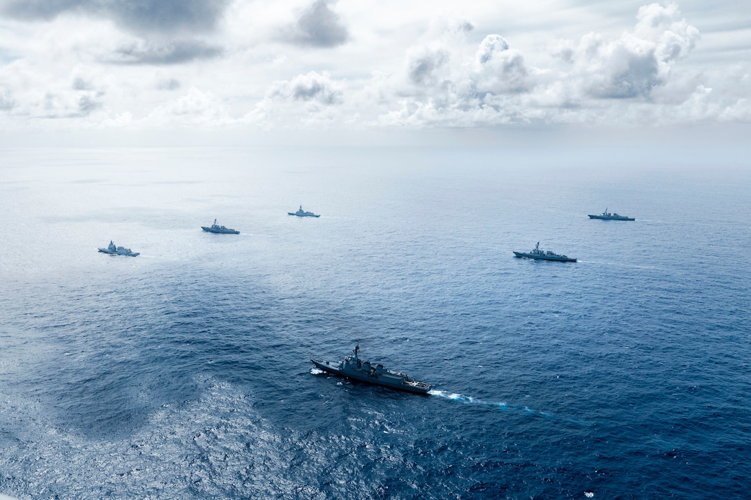 Six ships sail in formation under a cloudy sky.