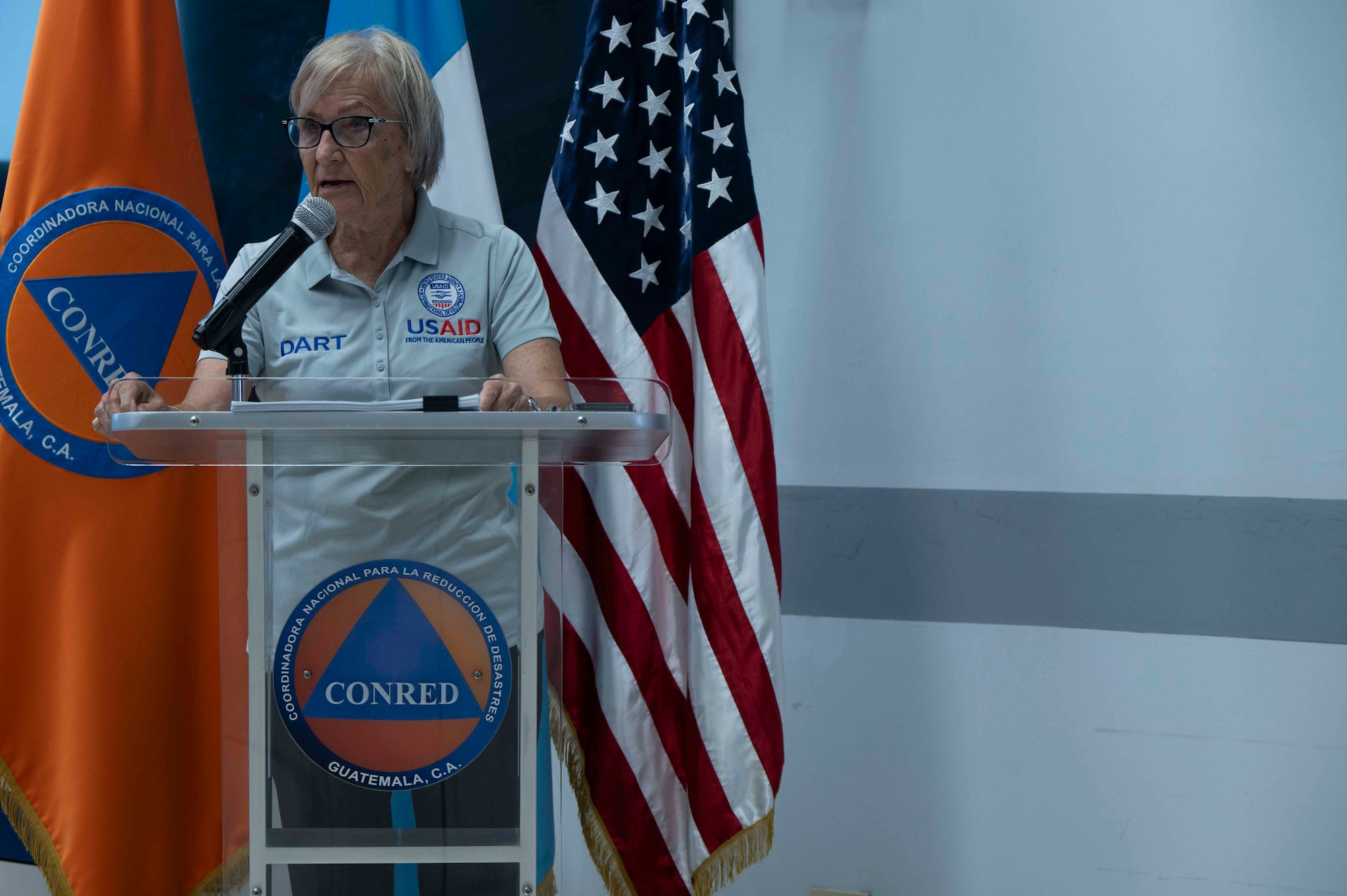 A photo of a woman in a USAID shirt speaking at a podium.