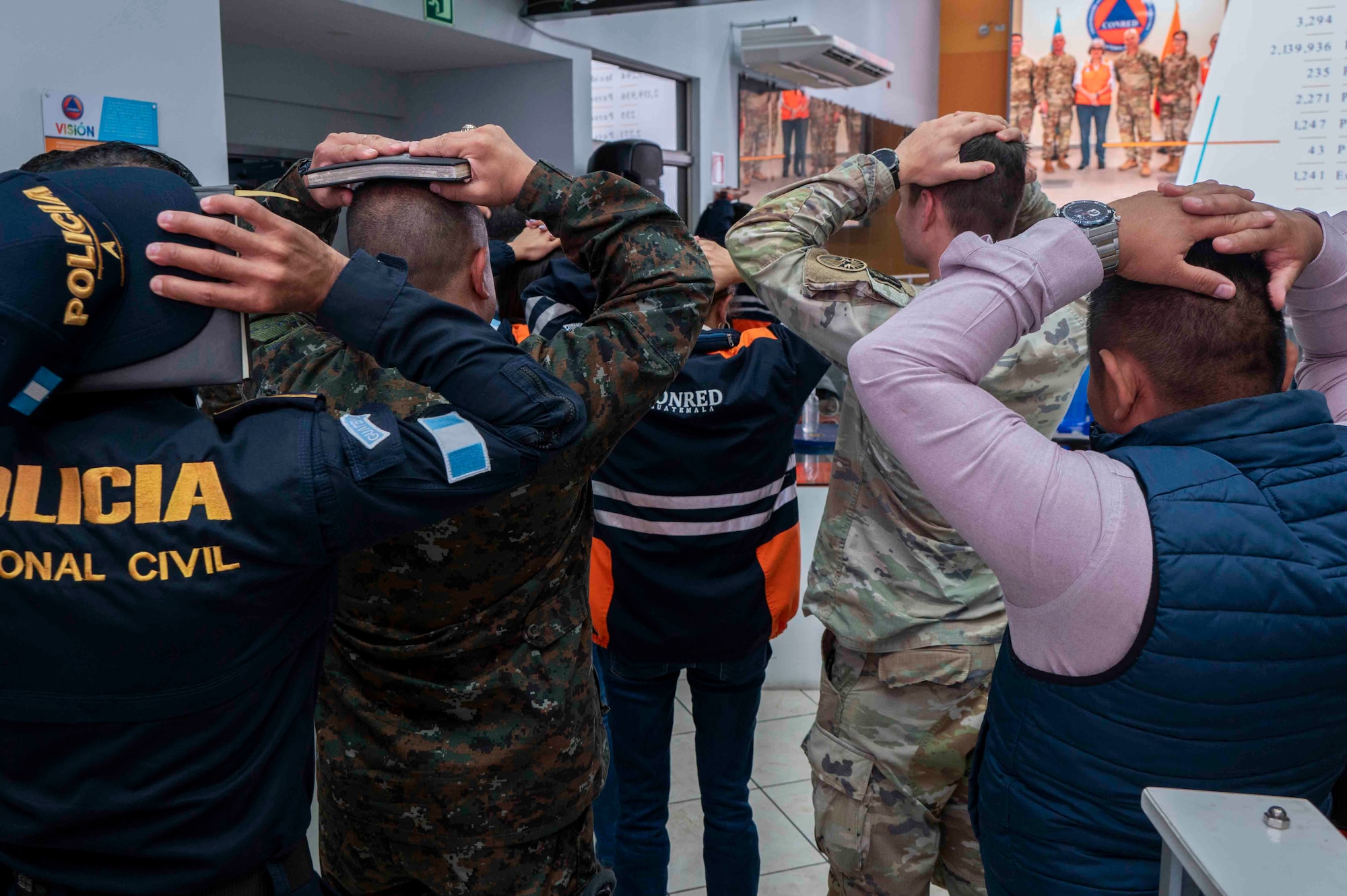 A photo of people walking out a door with their hands over their heads.