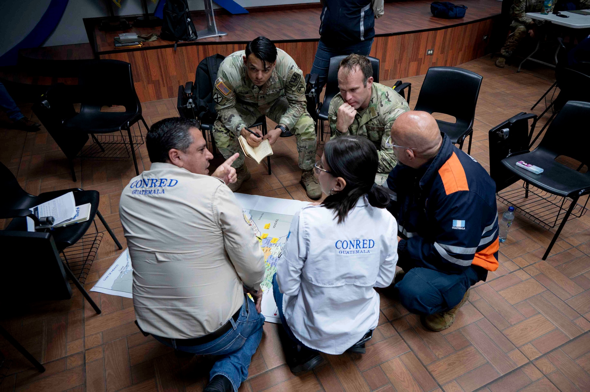 A photo of a group of people looking over a map on the floor while talking.