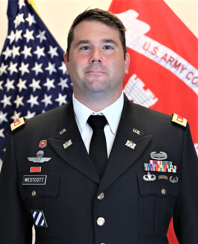 U.S. Army Officer in dress blue, class A uniform. Brown hair and brown eyes.