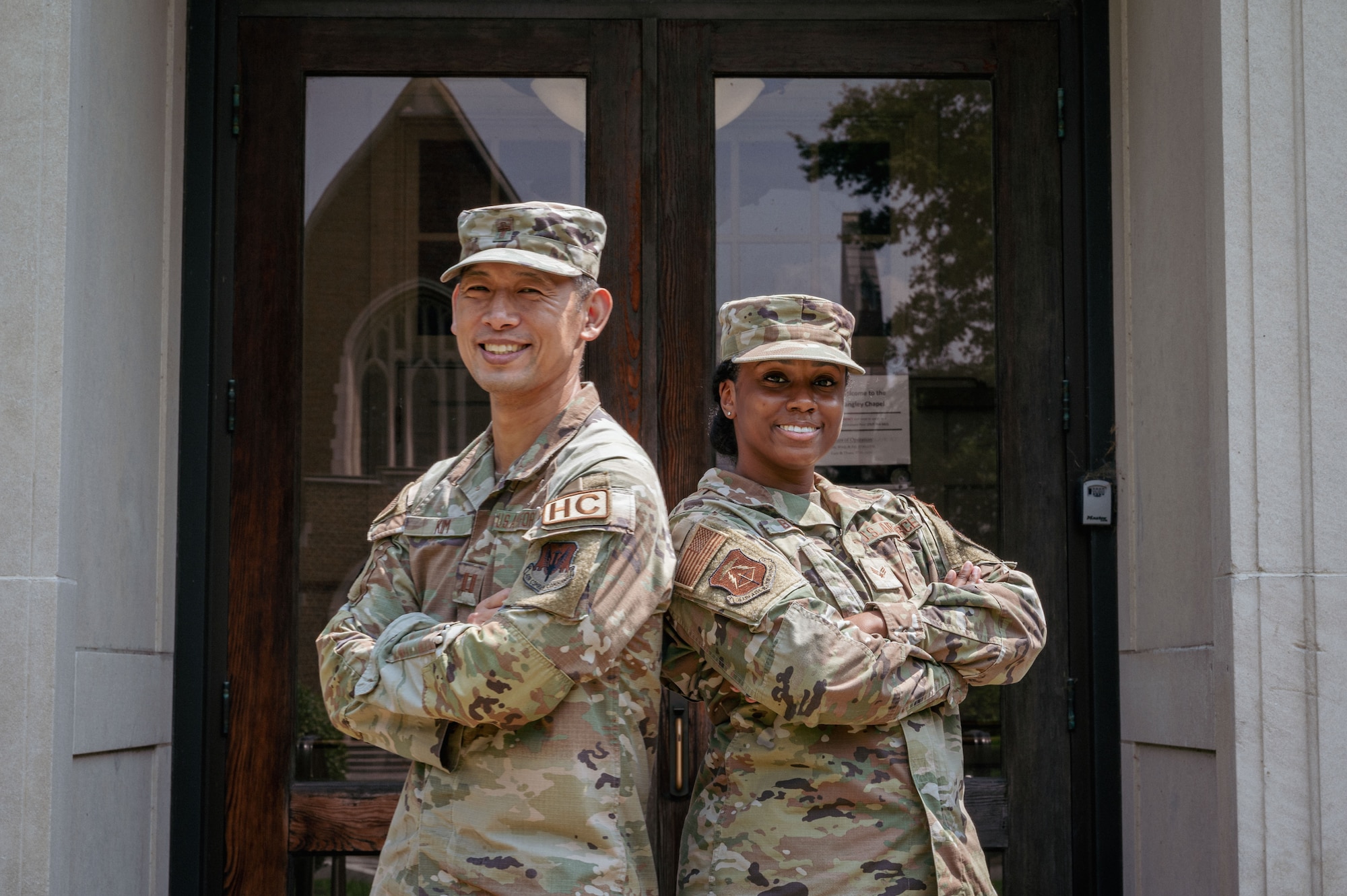 Two airmen stand back to back posed in front of doors.