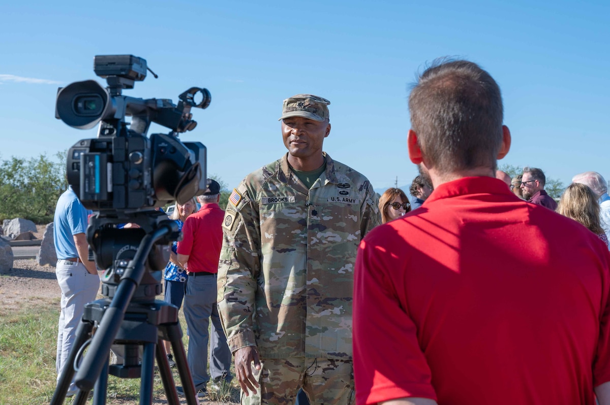 A man in a military uniform stands next to a camera.