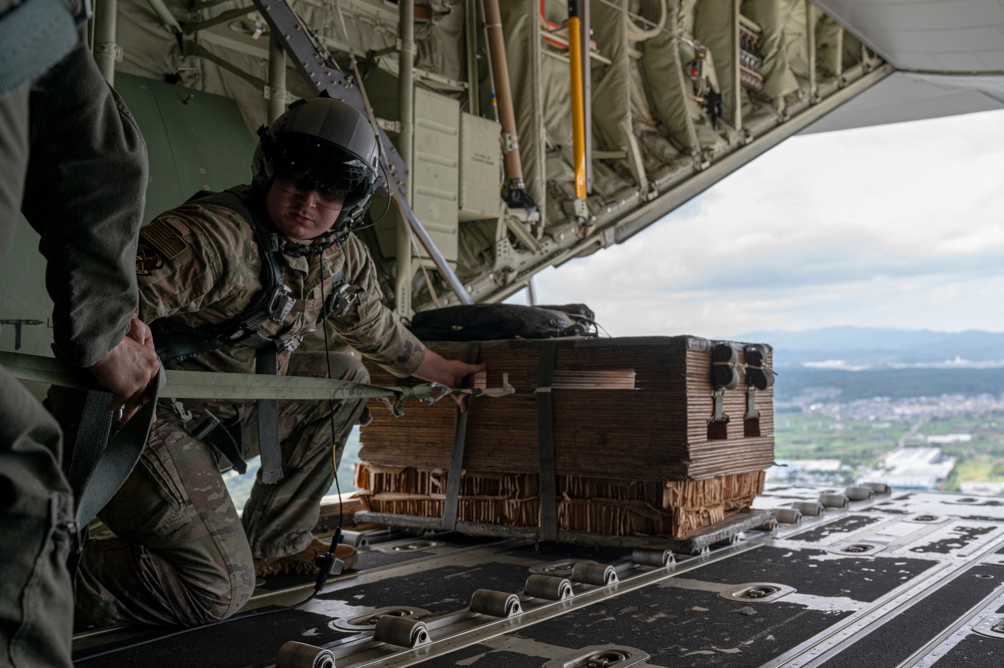 A loadmaster launches cargo out of the cargo ramp on an aircraft.