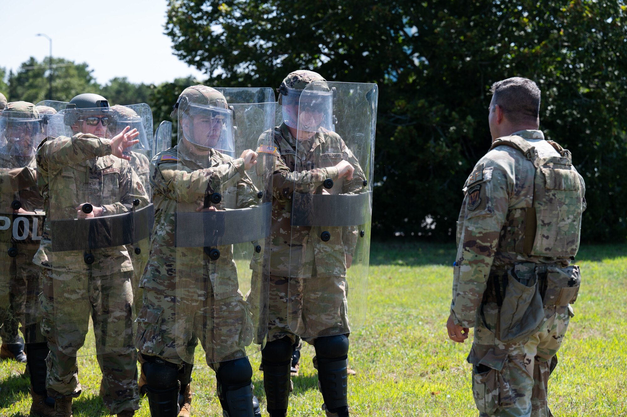 Airmen and Soldiers stand in a formation with helmets, shields and other protective gear
