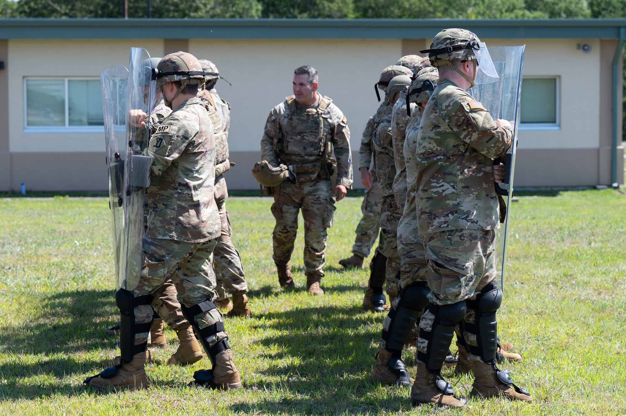 Airmen and Soldiers stand in a formation with helmets, shields and other protective gear