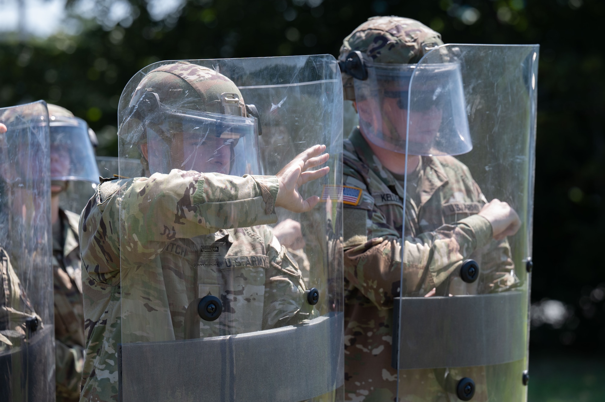 Airmen and Soldiers stand in a formation with helmets, shields and other protective gear