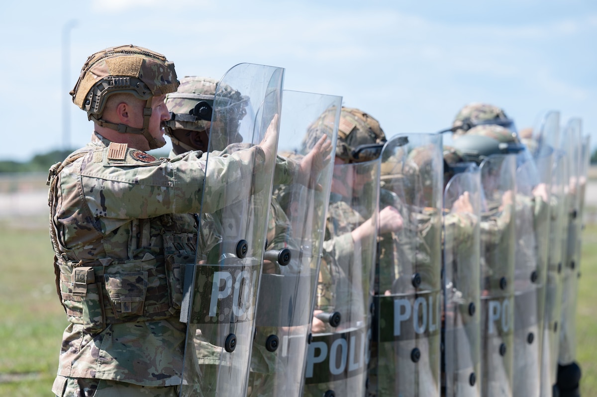 Airmen and Soldiers stand in a formation with helmets, shields and other protective gear