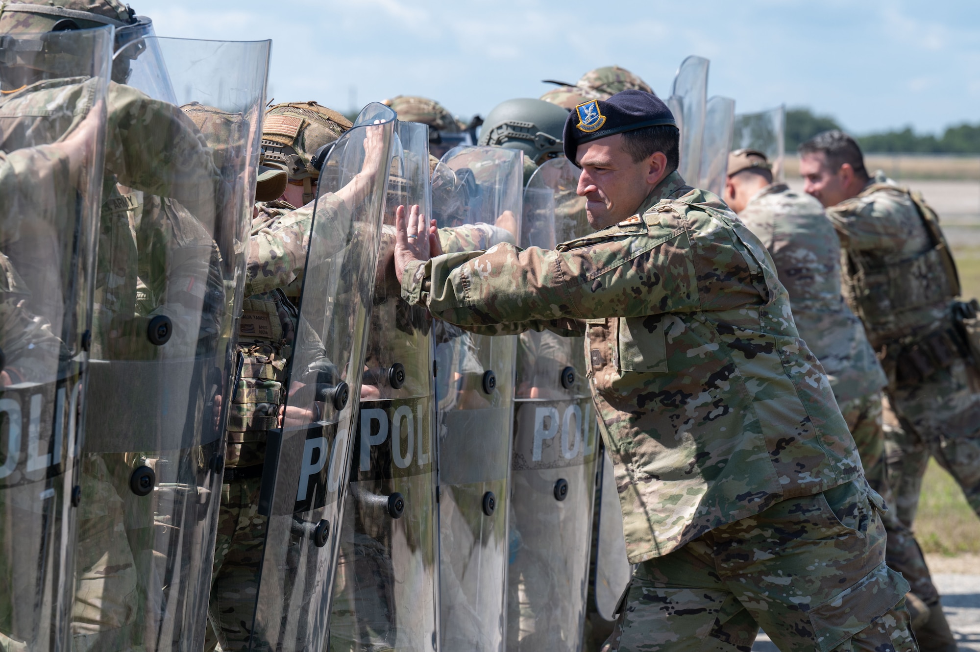 Airmen and Soldiers stand in a formation with helmets, shields and other protective gear