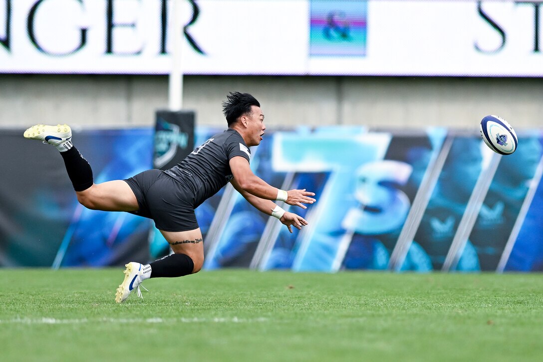 A soldier in athletic gear dives for a rugby ball during a match.