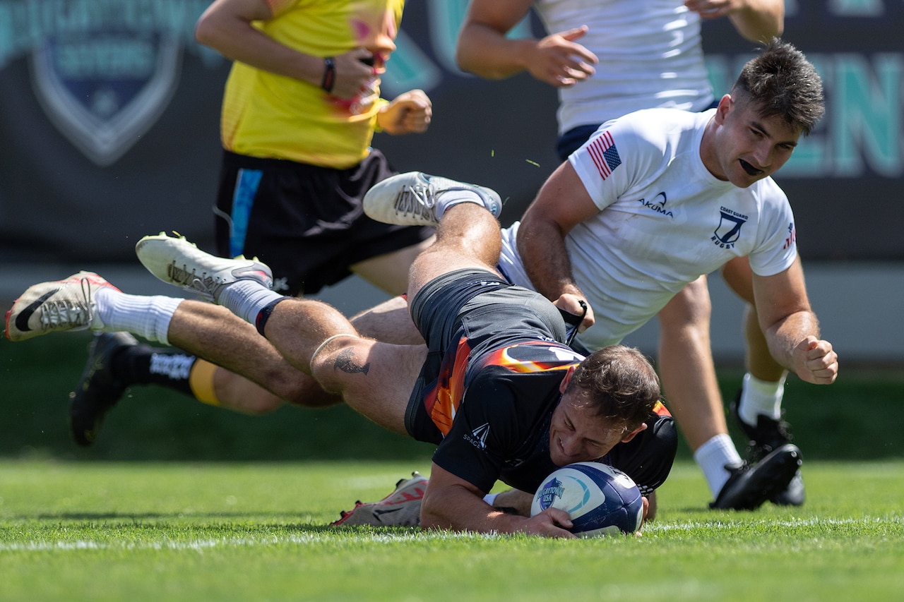 A player with a rugby ball falls to the ground with another player trying to tackle him.
