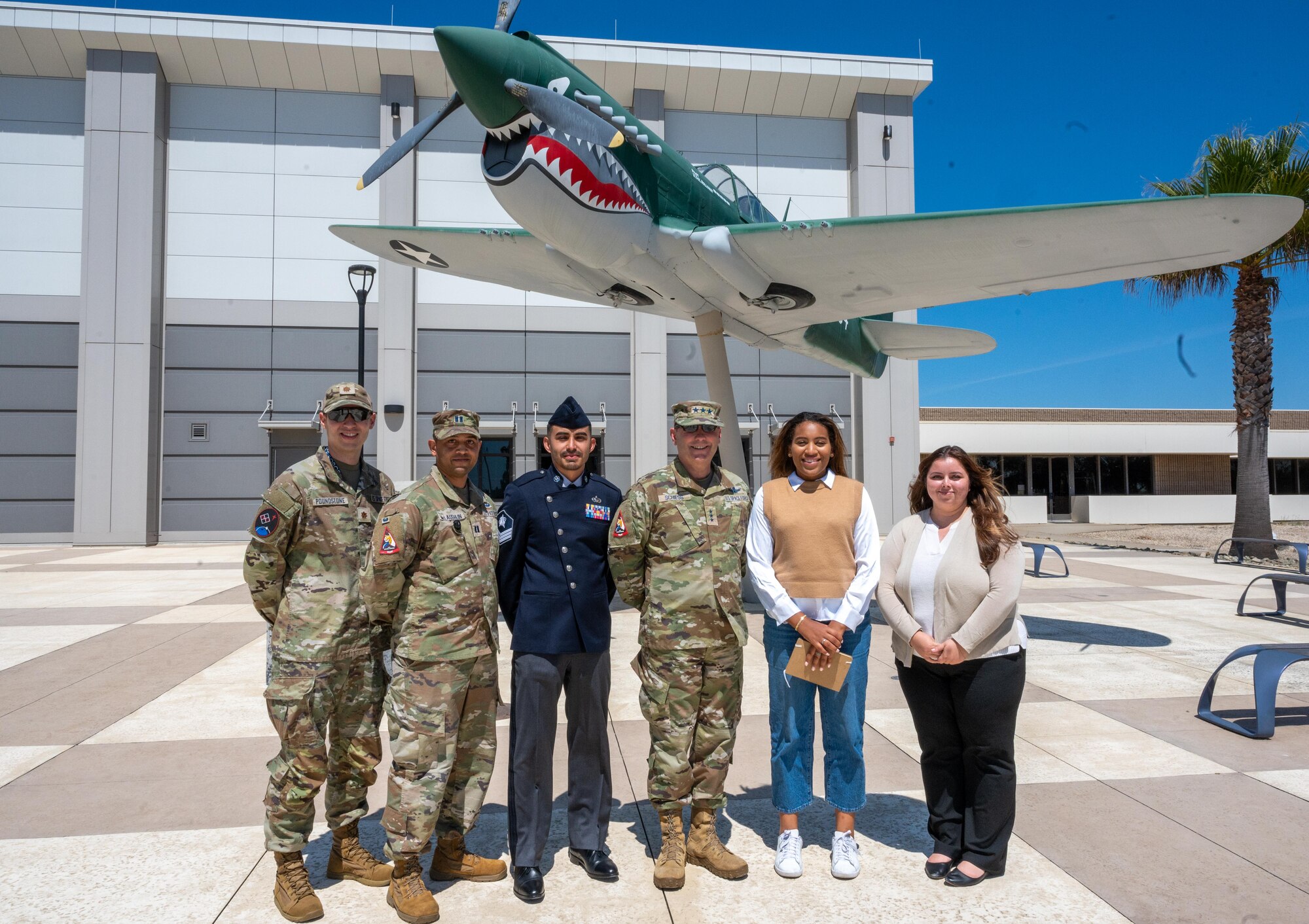 Military members and a congressional staff pose in front of a vintage warplane