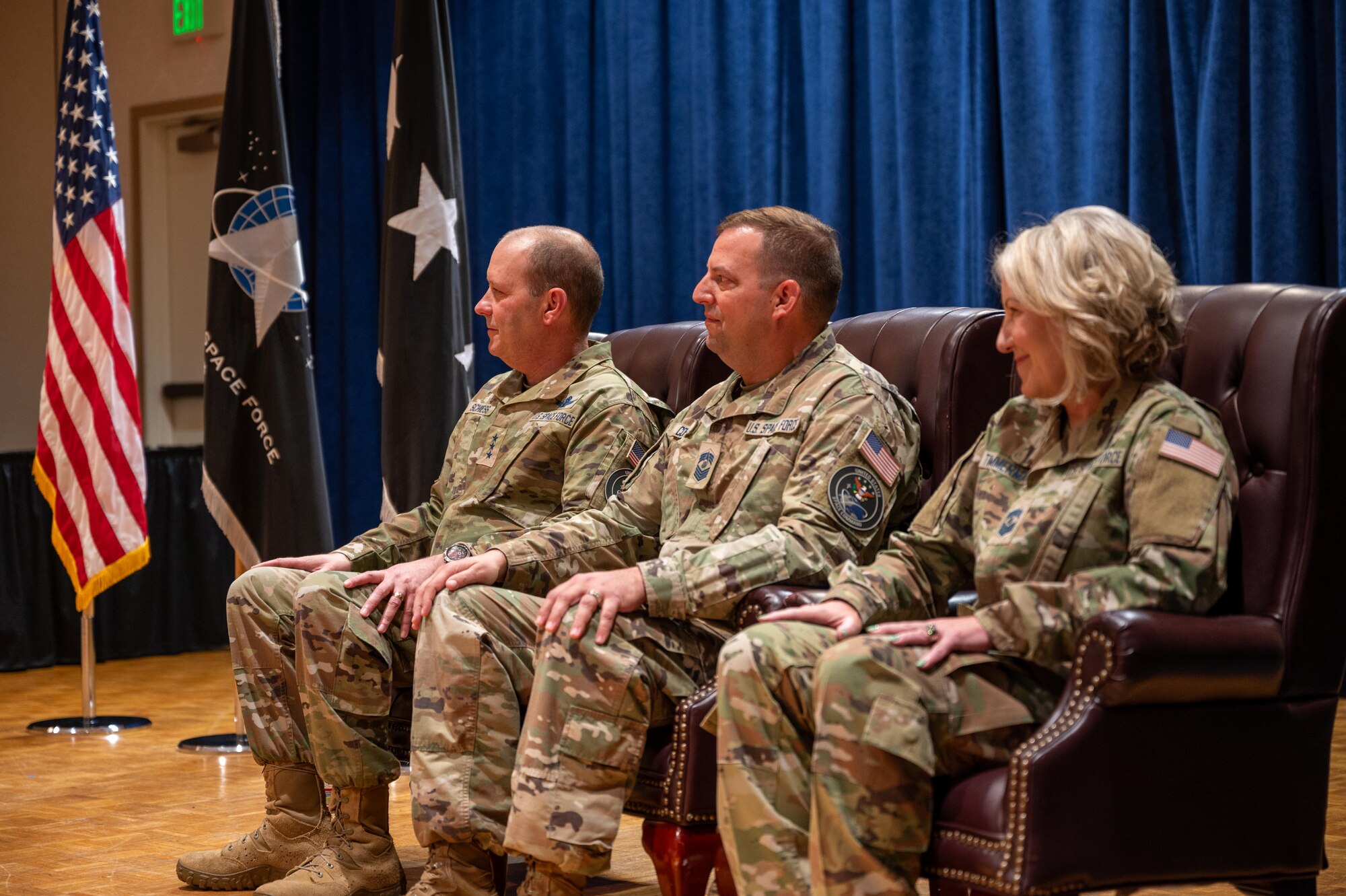 Three senior military soldiers listen as another speaks at an off-camera podium during an official ceremony.