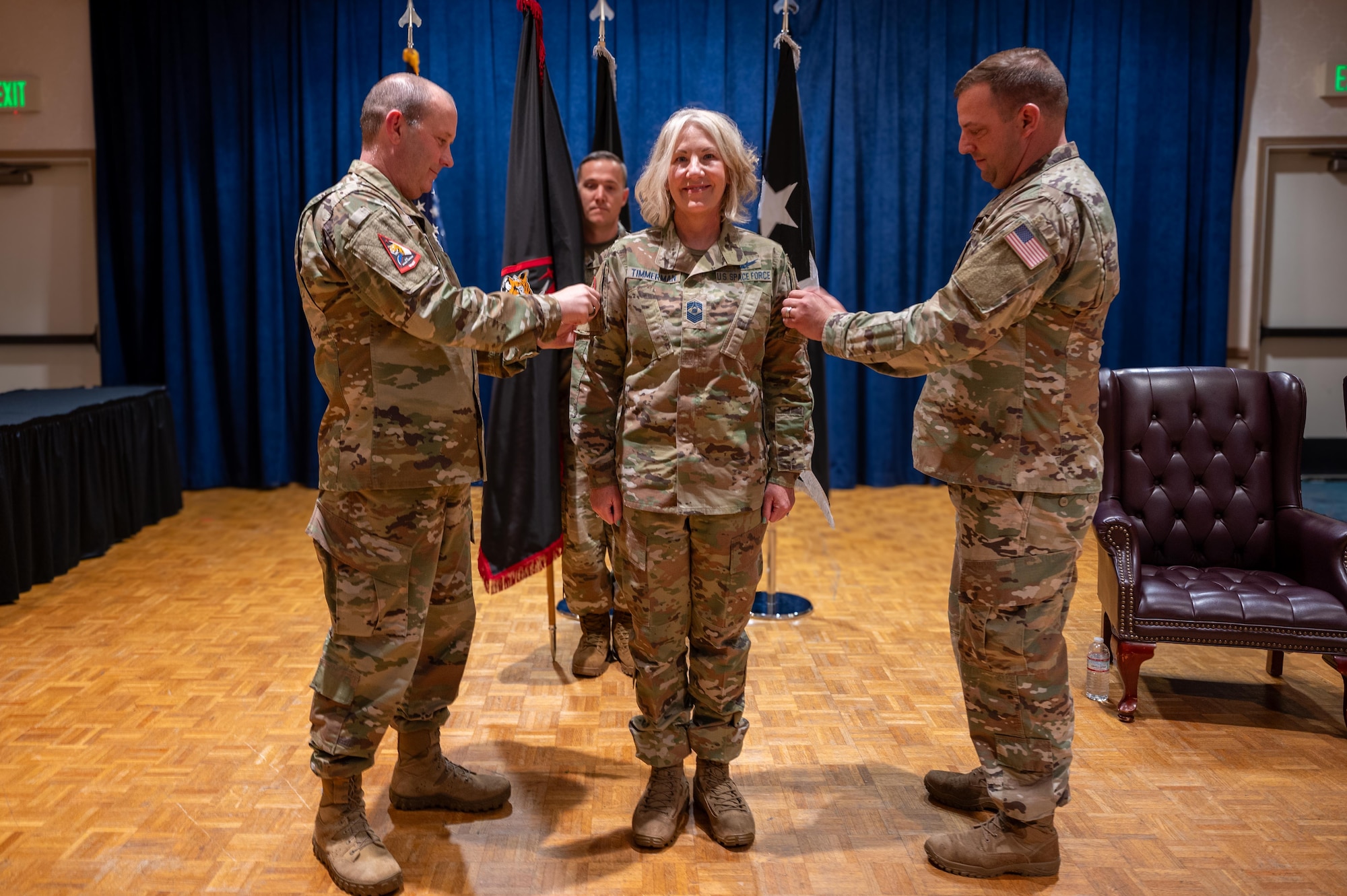 Two military members affix patches onto the shoulders of a third.