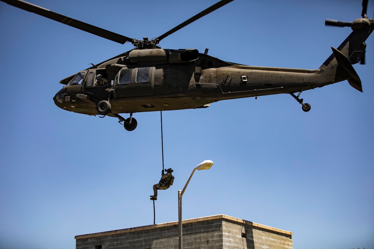 A soldier ropes out of a helicopter onto the roof of a cement building.