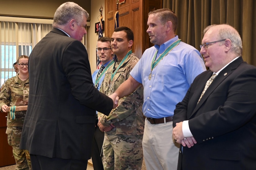 Col. Richard Spiegel, representing the Army Public Affairs Association, shakes hand with Brad Rhen, deputy state public affairs officer, after inducting him and the other members of the state public affairs office into the Order of St. Gabriel Aug. 20, 2024, at Fort Indiantown Gap, Pa. (U.S. Army National Guard photo by Spc. Jessica Barb)