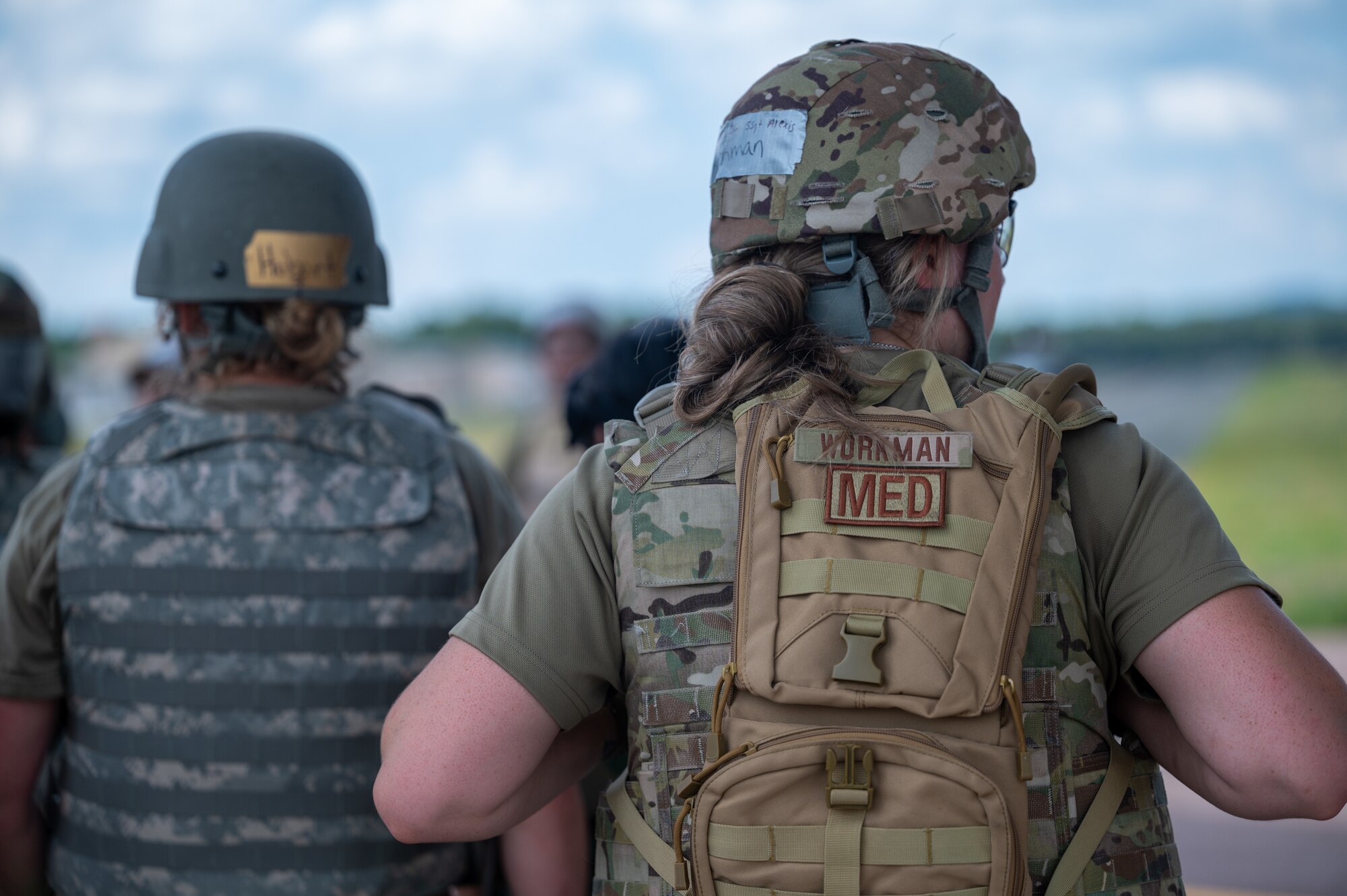 Staff Sgt. Alexis Workman's back is turned to camera with her duty identifier patch labeled "MED" showing prominently below her nametape on her backpack
