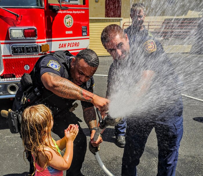 Officer Aerial Braswell, Department of the Air Force Civilian Police, 61st Security Forces Squadron, and a San Pedro firefighter hold a firehose to make a parking lot into a waterpark.