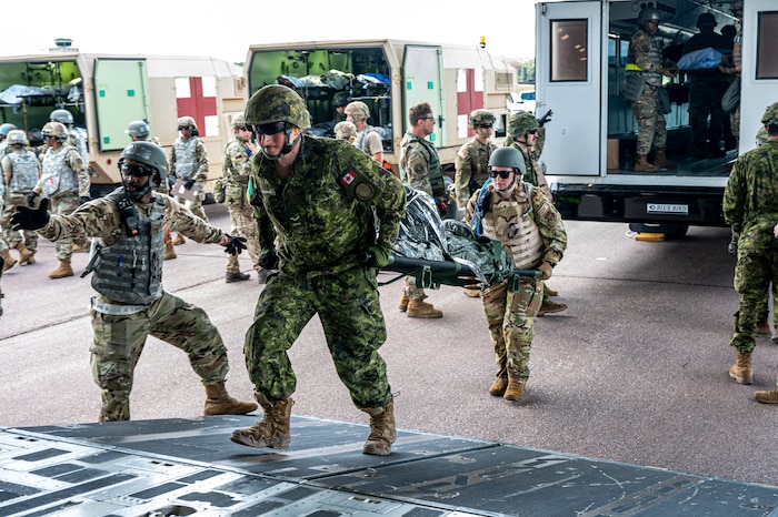U.S. Armed Forces and NATO Allied medical personnel perform patient movement aboard a C-17 Globemaster III as a Canadian and U.S. medic carry a litter on the ramp.