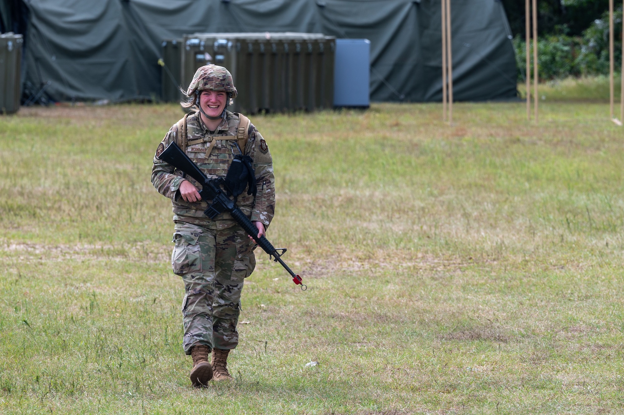 Staff Sgt. Alexis Workman smiles as she walks toward camera with a dummy weapon in hand as she enters entry control point duty