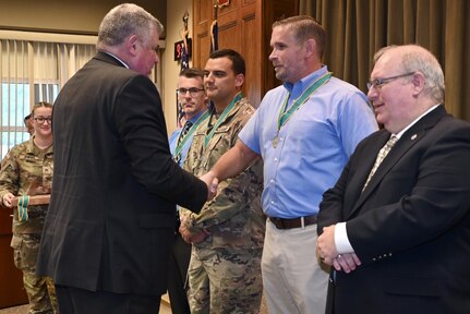 Col. Richard Spiegel, representing the Army Public Affairs Association, shakes hand with Brad Rhen, deputy state public affairs officer, after inducting him and the other members of the state public affairs office into the Order of St. Gabriel Aug. 20, 2024, at Fort Indiantown Gap, Pa. (U.S. Army National Guard photo by Spc. Jessica Barb)