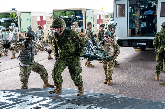 U.S. Armed Forces and NATO Allied medical personnel perform patient movement aboard a C-17 Globemaster III as a Canadian and U.S. medic carry a litter on the ramp.