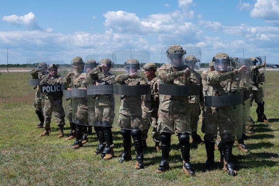 Airmen and Soldiers stand in a formation with helmets, shields and other protective gear