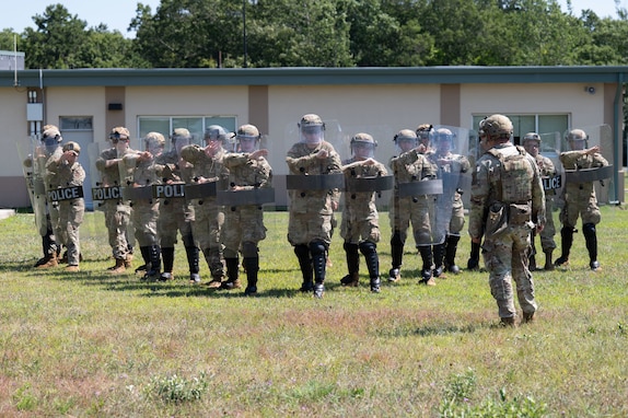 Airmen and Soldiers stand in a formation with helmets, shields and other protective gear