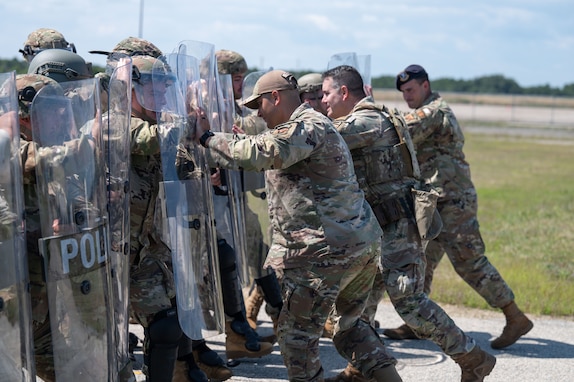 Airmen and Soldiers stand in a formation with helmets, shields and other protective gear