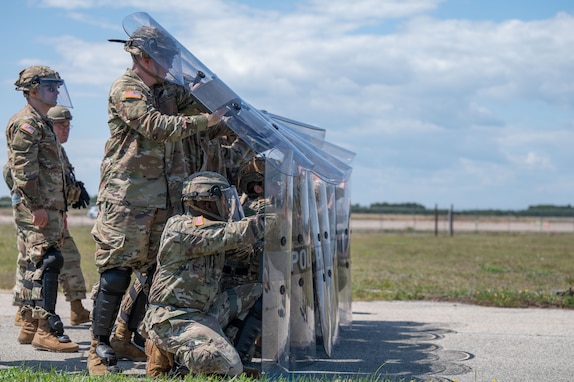 Airmen and Soldiers stand in a formation with helmets, shields and other protective gear