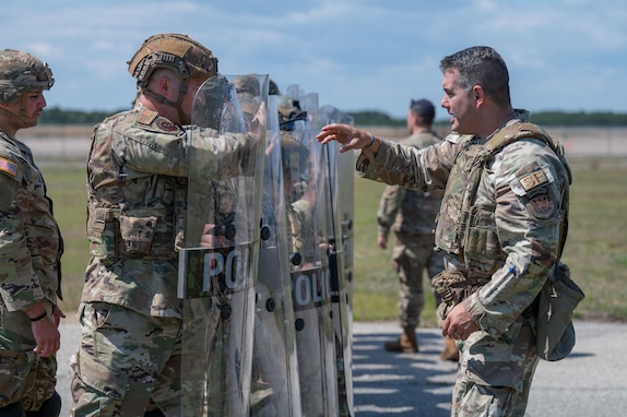 Airmen and Soldiers stand in a formation with helmets, shields and other protective gear