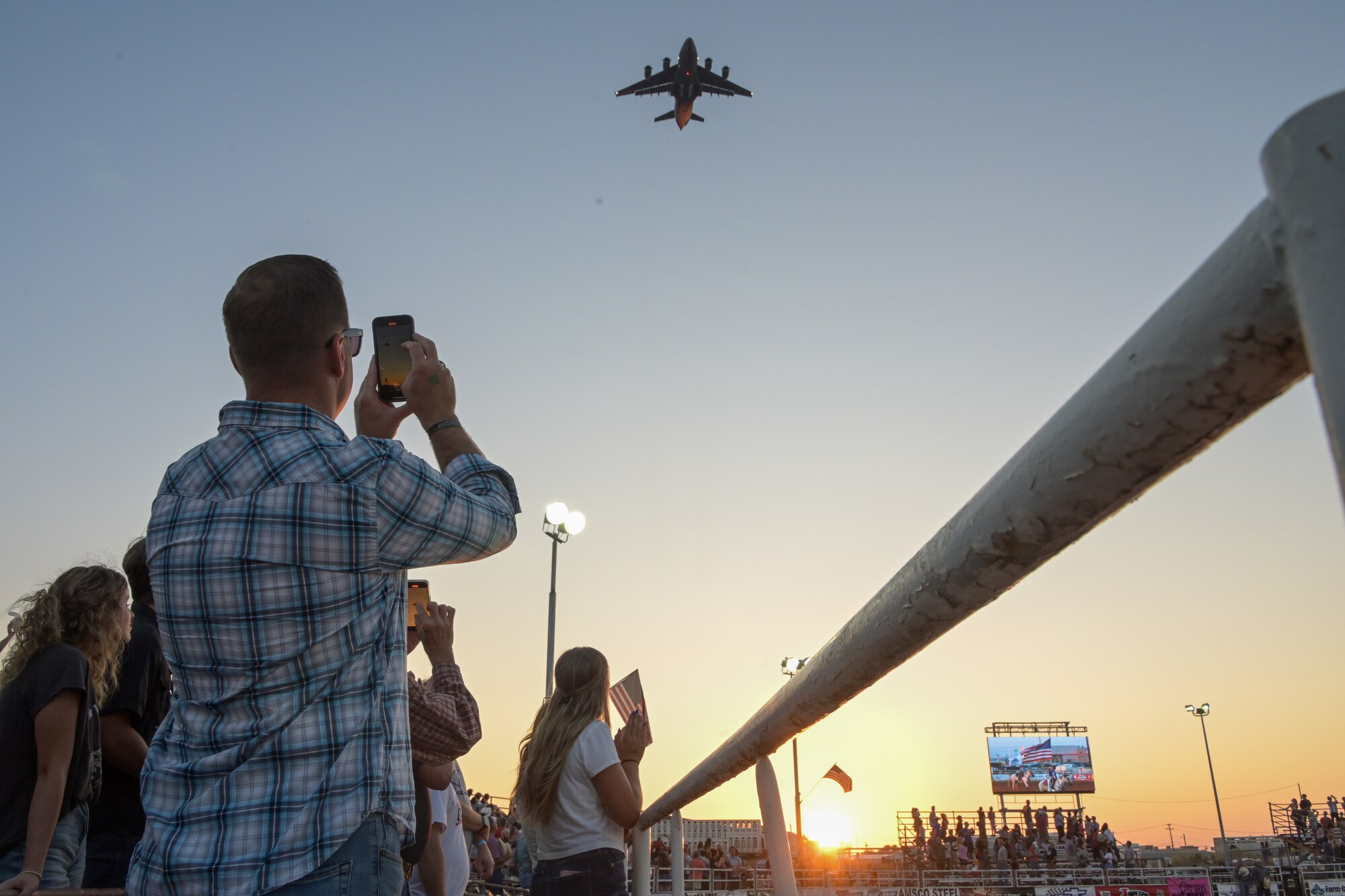 U.S. Air Force Chief Master Sgt. Keith Scott, 19th Air Force (AF) command chief, takes a photo of a C-17 Globemaster III aircraft flying over the rodeo at Altus, Oklahoma, Aug. 22, 2024. The 19th AF command team was recognized as honored guests during military appreciation night at the Great Plains Stampede Rodeo. (U.S. Air Force photo by Airman 1st Class Lauren Torres)