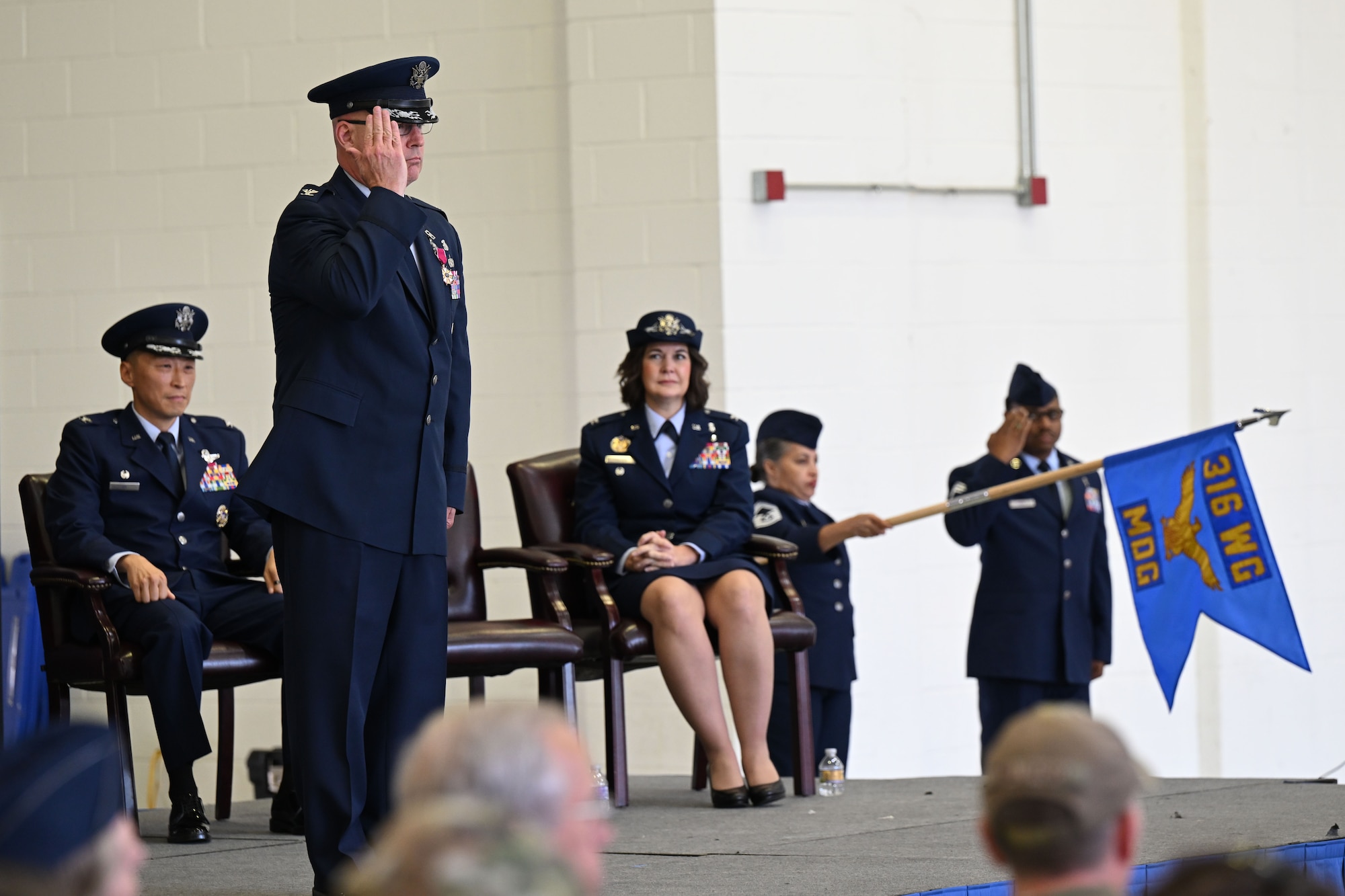 Military member salutes while standing on a stage.