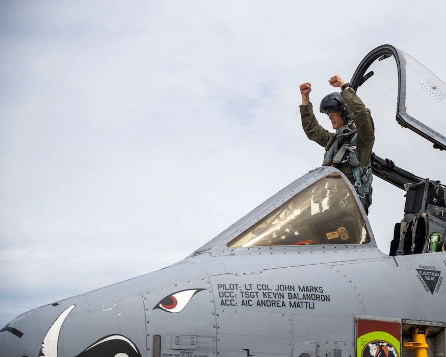 A man stands in the cockpit of an A-10 Thunderbolt II attack aircraft and pumps his fists in a sign of victory.