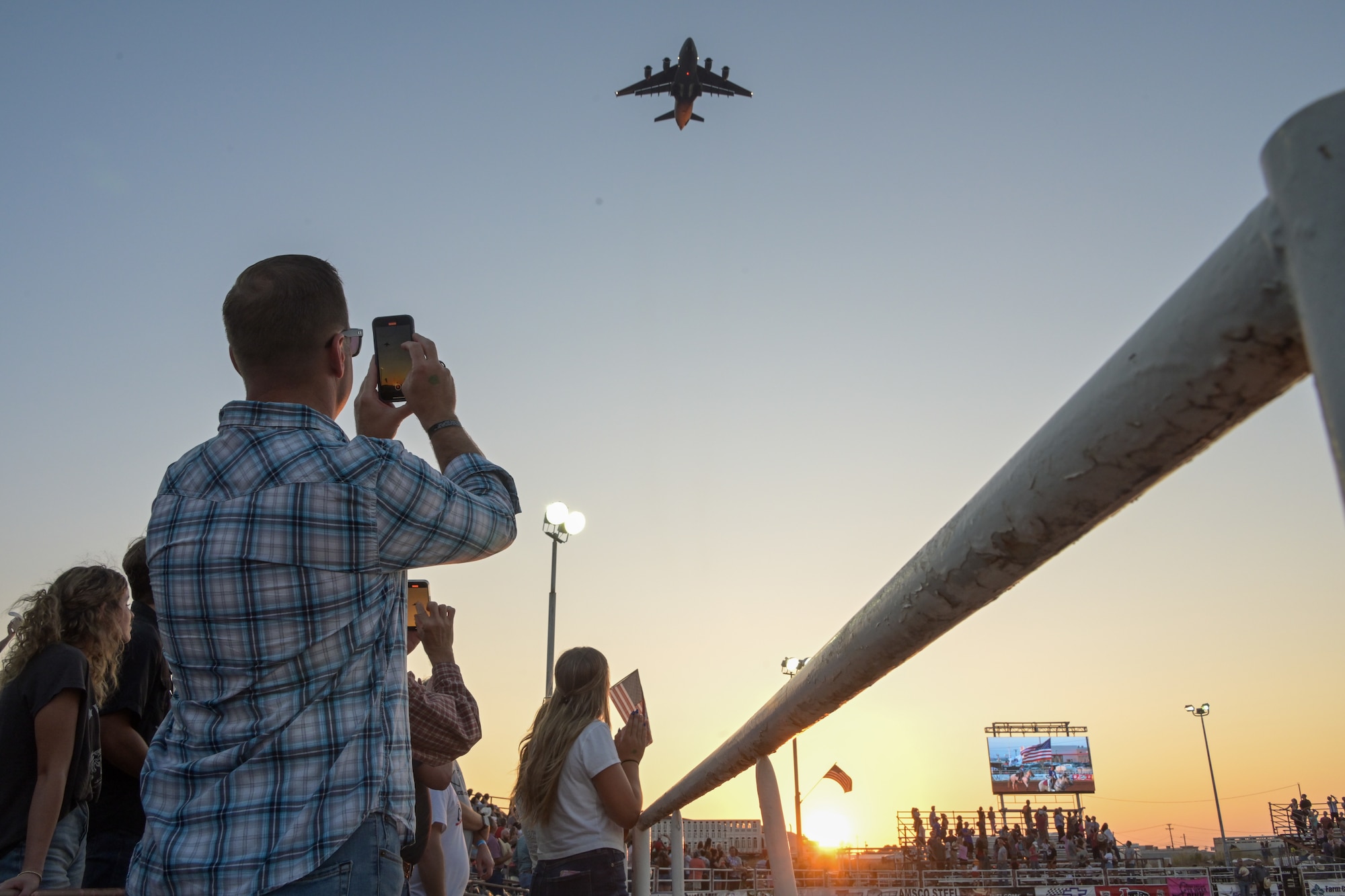 U.S. Air Force Chief Master Sgt. Keith Scott, 19th Air Force (AF) command chief, takes a photo of a C-17 Globemaster III aircraft flying over the rodeo at Altus, Oklahoma, Aug. 22, 2024. The 19th AF command team was recognized as honored guests during military appreciation night at the Great Plains Stampede Rodeo. (U.S. Air Force photo by Airman 1st Class Lauren Torres)