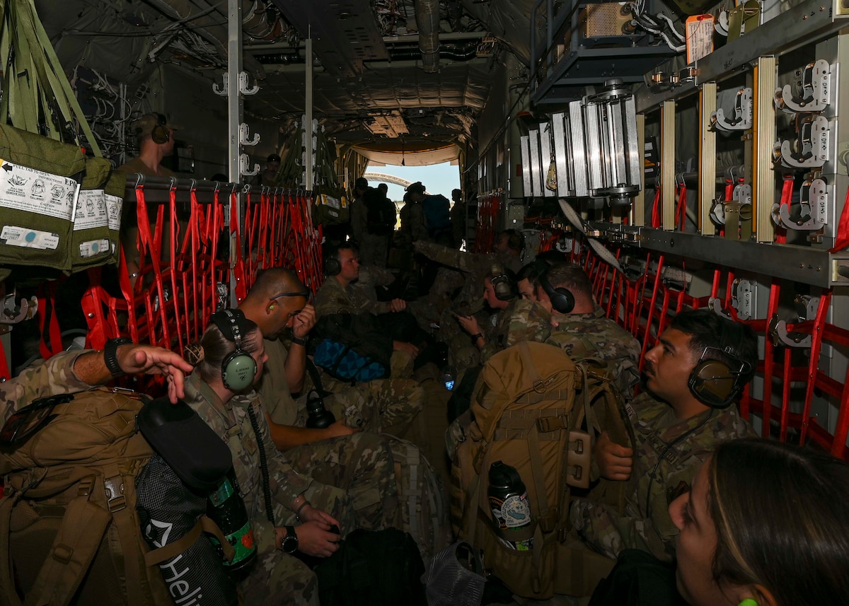 People in military uniforms sit in the cargo area of a plane