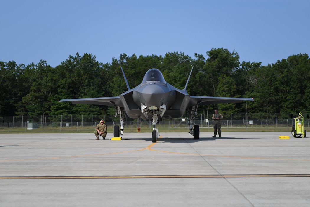 An F-35 lighting II aircraft faces camera, nose first with two Airmen standing on either side of it.